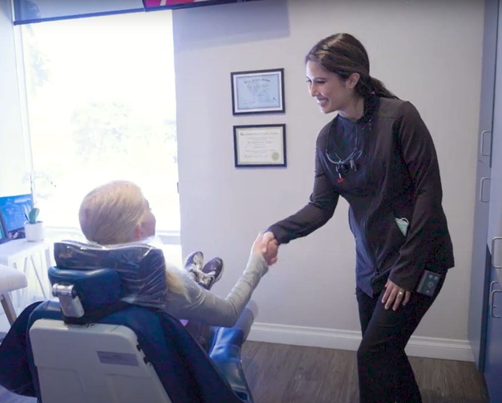 Dr. Etesse shaking hands with a young patient in the dental chair at her practice in Solana Beach